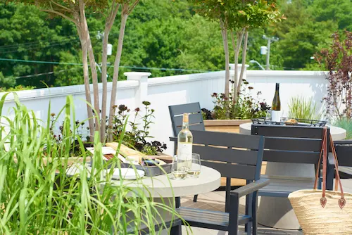 A patio with a table and chairs, featuring a bottle of wine and a plant.