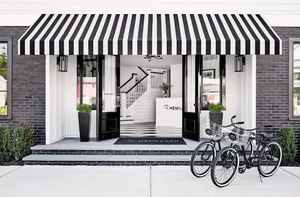 A storefront with a black and white striped awning, featuring a bicycle in front, a staircase, and a menu sign.