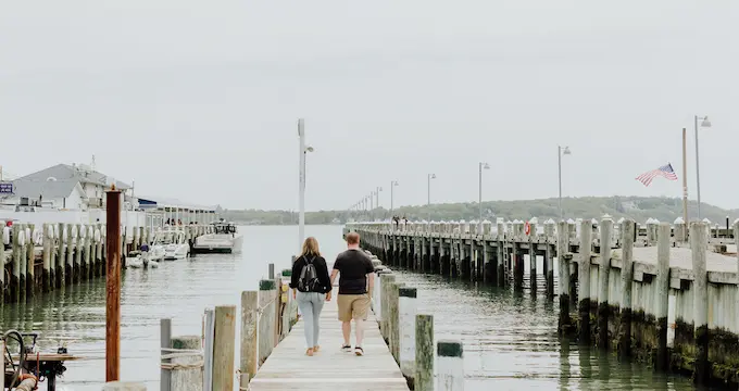 A person walking on a dock, possibly on a cloudy day, with a boat in the water.