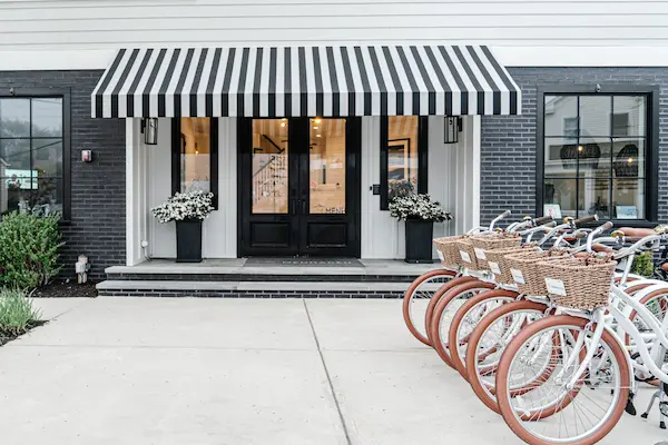 A row of bicycles parked in front of a storefront with a striped awning.