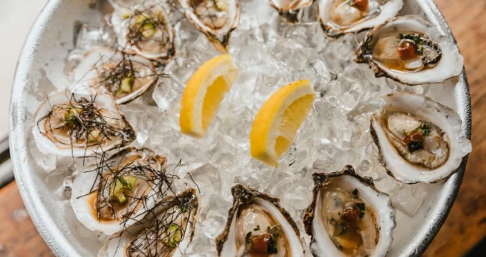 A plate of oysters on ice with lemon wedges, likely from a seafood restaurant menu.