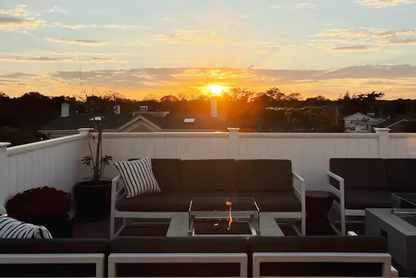 A rooftop patio with a couch, table, and plant, set against a sunset background.