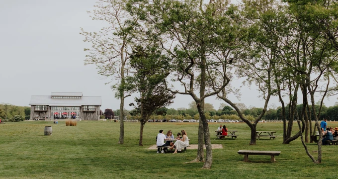 A park scene with a building, trees, and people sitting on the grass.