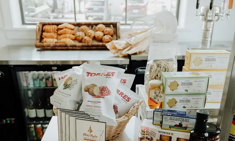 A basket of snacks on a counter with a window in the background. The basket contains bags of tortilla chips and other snacks.