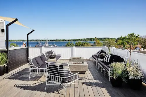 A modern rooftop patio with a white metal furniture set, overlooking a body of water.