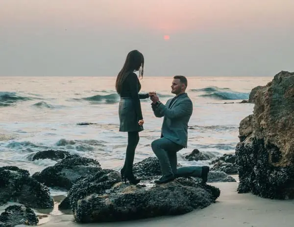 Man proposing to woman on a rocky beach at sunset.
