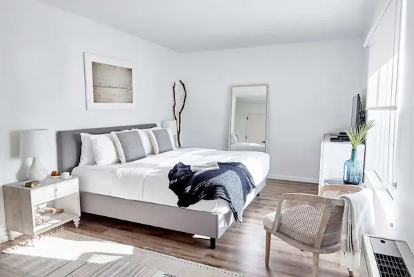 white bedroom with bed, nightstand, mirror, and chair.